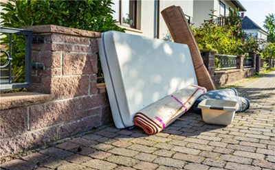 Photograph of a matress, carpets and bucket on a street